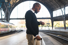 Black Businessman Checking Time On Wristwatch While Standing On Railway Platform