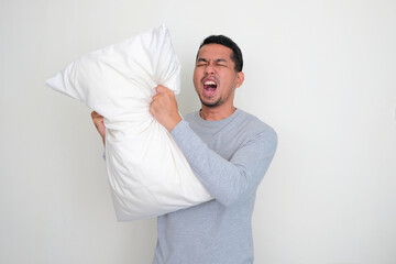 Wall Mural - Adult Asian man screaming angry while grabbing his sleeping pillow