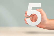 Number Five In Hand. Hand Holding White Number 5 On Blurred Background With Copy Space. Concept With Number Five. Birthday 5 Years, Fifth Grade, Five Day Work Week