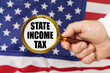 In front of the American flag, a man holds a magnifying glass in his hand with the inscription - state income tax