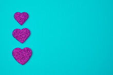 Three Glittering Purple Magenta Hearts On Blue Green Turkuoise Background. Valentines Day Concept. Copy Space. Flat Lay.