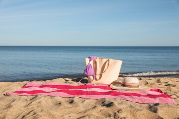 Poster - Beach towel with bag, straw hat and bikini on sand near sea, space for text