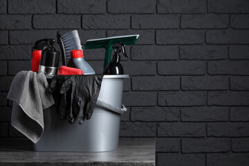 Different car cleaning products in bucket on table near black brick wall, space for text