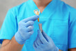 Dentist holding educational model of dental implant on blurred background, closeup