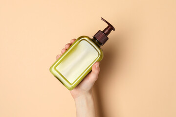 Sticker - Woman holding shampoo bottle on beige background, top view