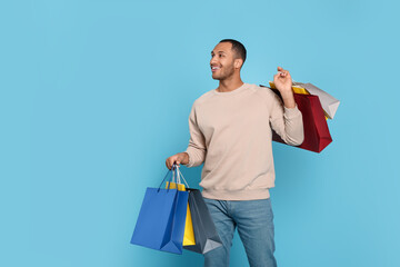 Happy African American man with shopping bags on light blue background