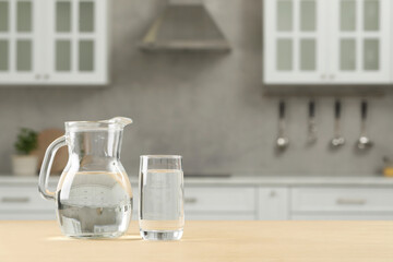 Wall Mural - Glass and jug with water on wooden table in kitchen, space for text