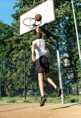 Cute young teenager in t shirt with a ball plays basketball on court. Teenager running in the stadium.  Sports, hobby, active lifestyle for boys