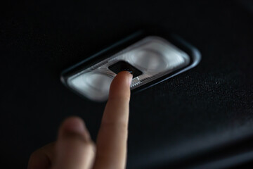 Close up a small finger from little 5 years old girl raises hand up to turn on and turn off car lamp at the back seat ceiling inside the car.