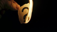A Man Burns Paper With A Question Mark In The Dark.