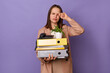 © sementsova321 - Portrait of sad unhappy young adult woman wearing beige jacket holding lot of documents folders isolated over purple background, rubbing her eyes, crying, standing with her office stuff in hands.