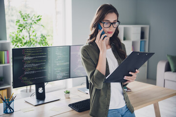 Photo of serious confident lady administrator wear spectacles talking modern device looking list indoors workplace workshop