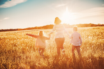 Mother with her children running on the field on the summer sunset.