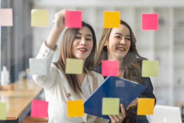 Wall Mural - Team of Business female employee with many conflicting priorities arranging sticky notes commenting and brainstorming on work priorities colleague in a modern office.