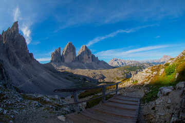 Wall Mural - Mountain valley on a sunny day with clouds. Landscape with a bridge, high rocks, colorful blue sky, clouds, sunlight. Mountains in Tre Cime park in Dolomites, Italy. Italian alps.