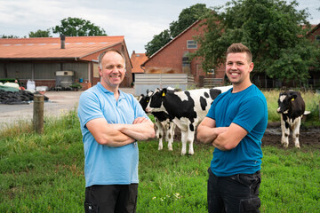 Poster - Zwei Landwirte auf einer Wiese mit Rindern, im Hintergrund Hofgebäude.