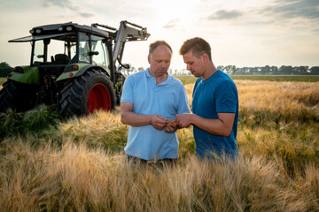 Poster - Landwirt mit seinem Sohn im reifen Getreidefeld, im Hintergrund steht ein Traktor.