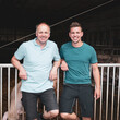 Vater und Sohn, beide Landwirte stehen vor einer Schweinebucht.