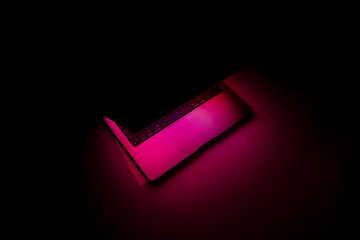 Laptop with backlit keyboard at night. Copy space. Illuminating pink neon light. Abstract horizontal poster about privacy information, security and technology