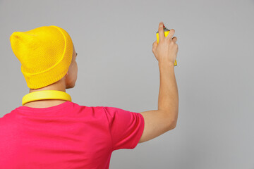 Wall Mural - Back view young man of African American ethnicity 20s he wears pink t-shirt yellow hat headphones hold in hand paint spray bottle look camera isolated on plain grey background Urban lifestyle concept.