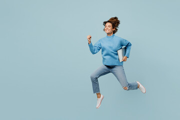 Full body side view fun surprised smart young IT woman wear knitted sweater hold closed laptop pc computer run fast isolated on plain pastel light blue cyan background studio People lifestyle concept.