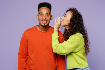 Wall Mural - Young couple two friends family man woman of African American ethnicity wear casual clothes together whisper gossip and tells secret behind her hand sharing news isolated on plain purple background