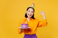 Happy Fun Overjoyed Young Woman Wears Casual Clothes Hat Celebrating Hold In Hand Purple Cake With Candles Do Winner Gesture Isolated On Plain Yellow Background. Birthday 8 14 Holiday Party Concept.