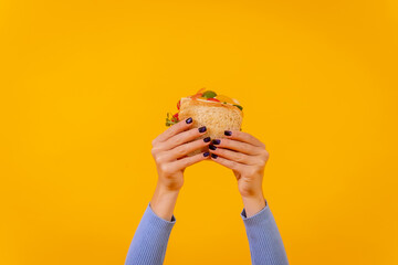 Hands of a woman with a sandwich on a yellow background, healthy food