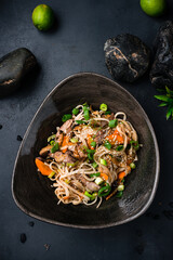 Wall Mural - Udon noodles with teriyaki beef and vegetables: red pepper, tomatoes, onion and sesame seeds.