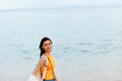 © SHOTPRIME STUDIO - Woman smile with teeth after swimming in the ocean with a backpack in a wet yellow tank top and denim shorts walks along the beach, summer vacation on an island by the ocean in Bali sunset