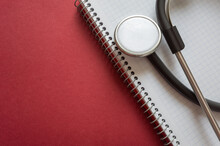 Doctor's Working Table With Stethoscope, Blank Medical Record Chart Or Test Results On Clipboard On A Red Background.