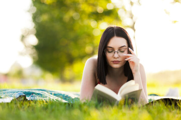 Beautiful girl lying in a park with a book. Outdoor leisure activity on a sunny summer day.