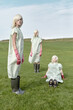 © Clique Images - Conceptual portrait of identical young blond women in clothing cover bags, rubber boots and pink gloves posing on green lawn and looking at camera