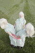 © Clique Images - Conceptual photo of young mysterious women with white blonde hair wearing garment covers standing on green lawn in circle embrace