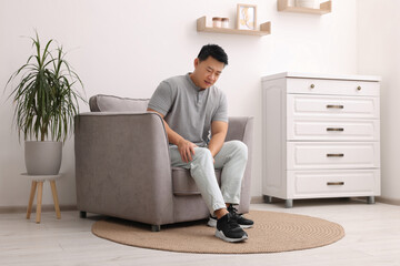 Poster - asian man suffering from knee pain on armchair indoors