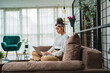 © Dusan - A young girl studying or doing business from her home while sitting on sofa and working on her laptop and drinking coffee during the day