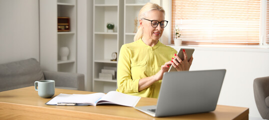 Wall Mural - Mature female psychologist with tablet computer and laptop sitting at table in office