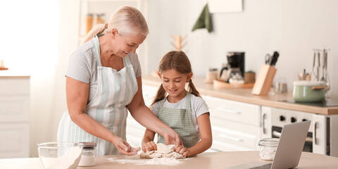 Wall Mural - Mature woman and her little granddaughter making dough in kitchen