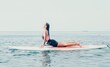 © panophotograph - Woman sup yoga. Happy young sporty woman practising yoga pilates on paddle sup surfboard. Female stretching doing workout on sea water. Modern individual female outdoor summer sport activity.