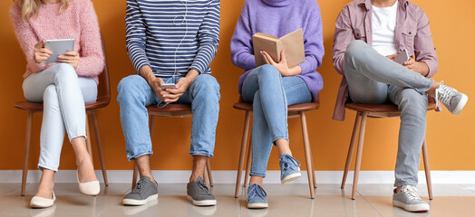 Poster - People waiting in line while sitting near orange wall