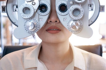 Pretty young woman having her eyes examined with optical Phoropter during eye exam, diagnostic ophthalmology equipment