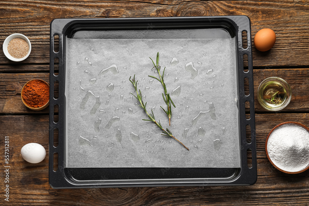 Baking tray with paper and ingredients on dark wooden background
