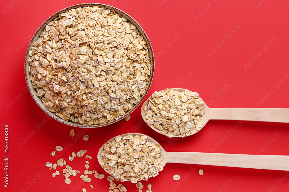 Bowl and spoons of raw oatmeal on red background
