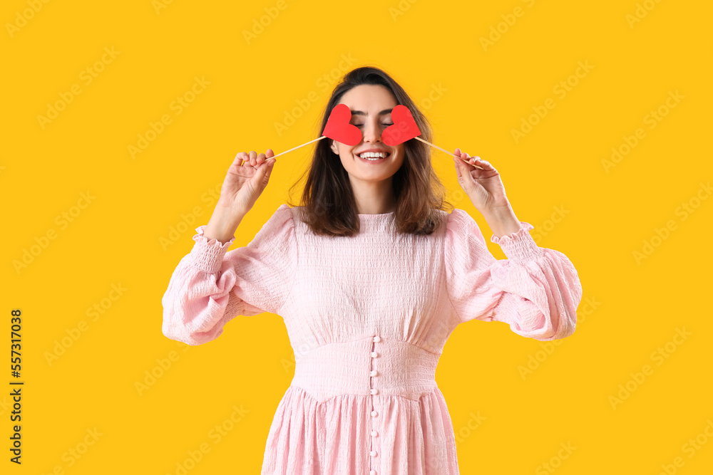 Young woman with paper hearts on yellow background. Valentine's Day celebration