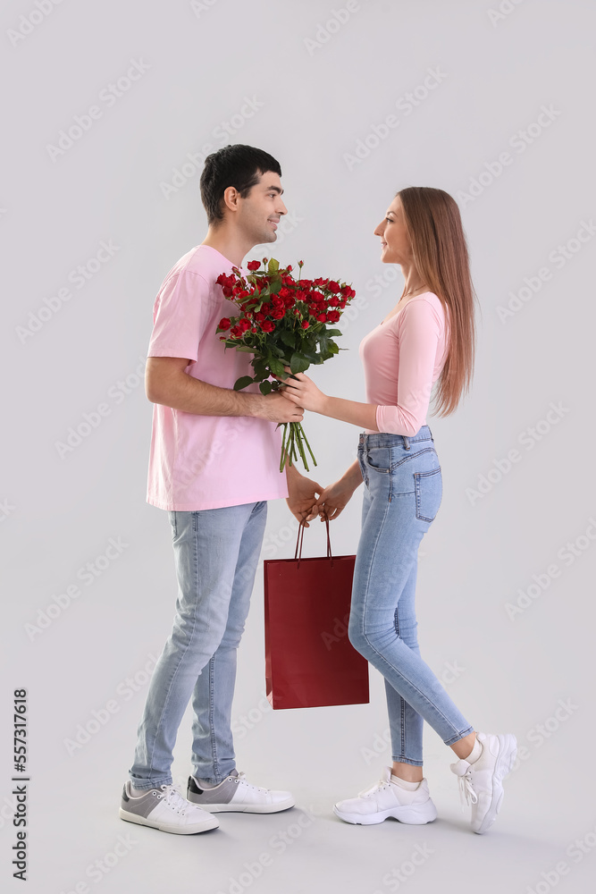 Young couple in love with roses and bag on light background. Valentine's Day celebration