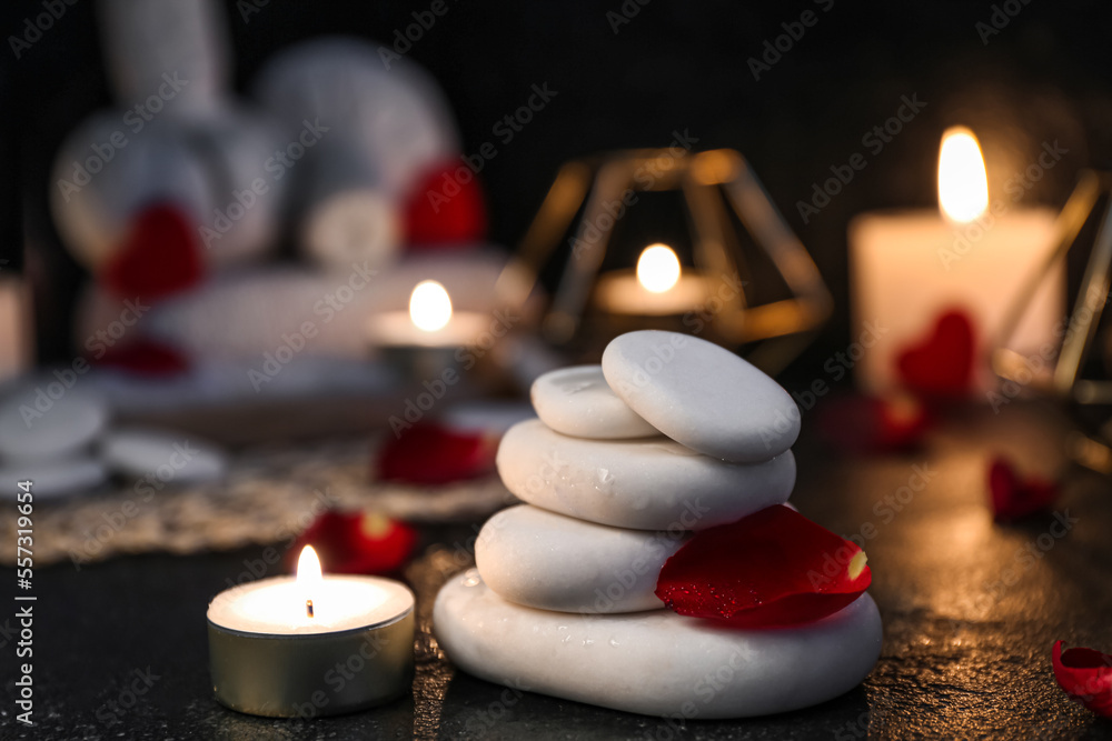 Spa stones with rose petal and candle on dark table, closeup. Valentine's Day celebration