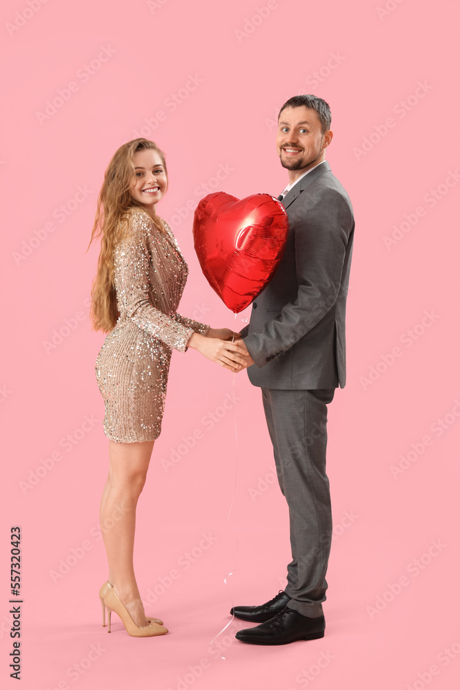 Happy young couple with heart-shaped balloon on pink background. Valentine's Day celebration