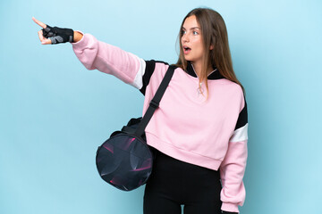 Wall Mural - Young sport woman with sport bag isolated on blue background pointing away