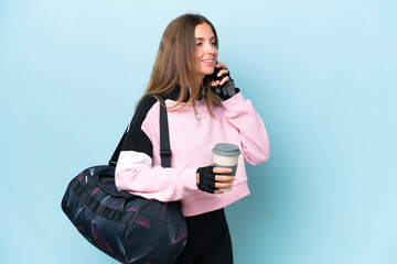 Wall Mural - Young sport woman with sport bag isolated on blue background holding coffee to take away and a mobile