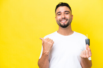 Young Arab man holding car keys isolated on yellow background pointing to the side to present a product